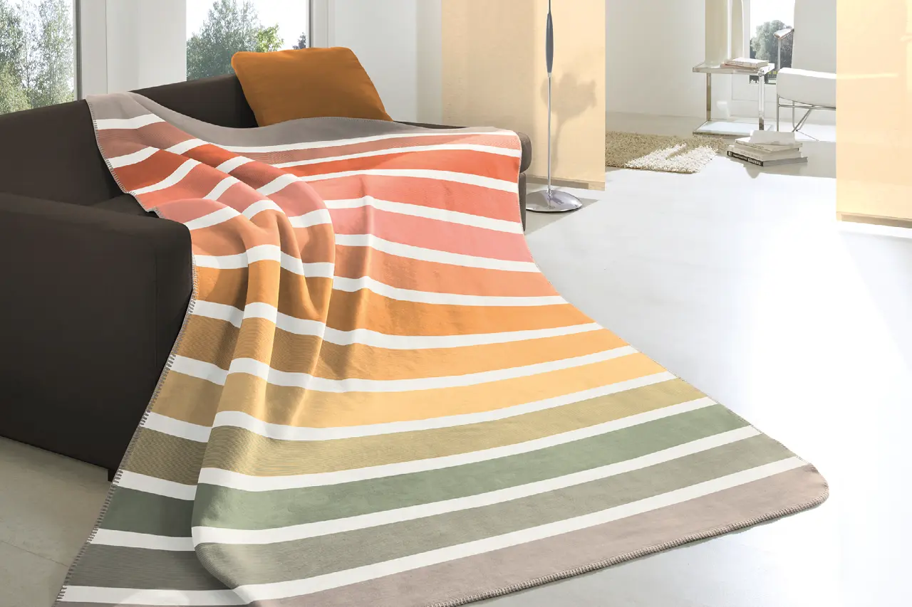 Gestreifte Kuscheldecke in warmen Farben auf modernem Sofa im Wohnzimmer, hochwertige Wohndecke als Wohnaccessoire für gemütliche Einrichtung und stilvolle Wohnraumgestaltung